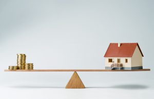 Model house and money coins balancing on a seesaw