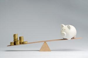 Money coins and piggy bank balancing on a seesaw