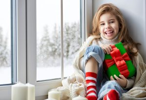 little girl sitting by the window with a gift and looking at the winter forest